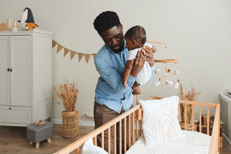 Un padre affettuoso che mette dolcemente il suo bambino in una culla accogliente, mostrando calore e cura familiare.