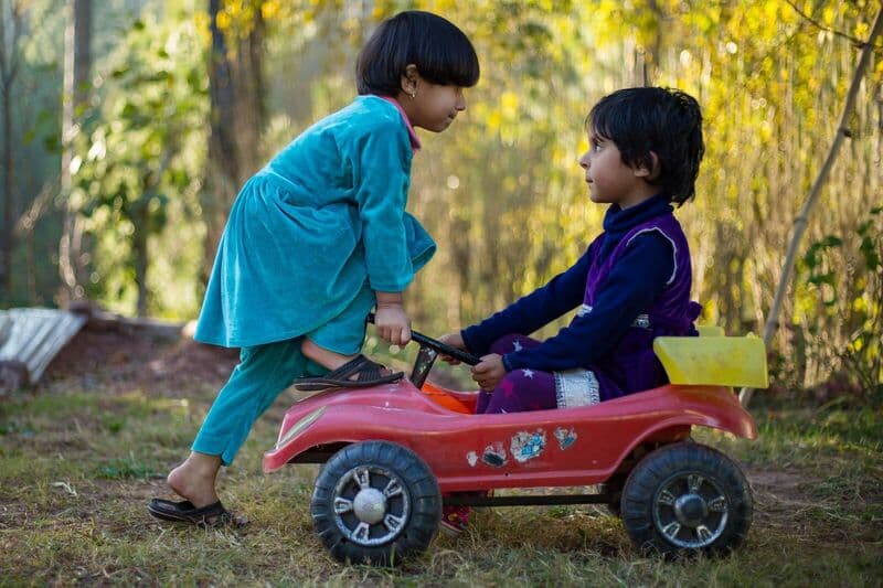 Due bambini che si godono una giornata di sole all'aperto con un'auto giocattolo, mostrando innocenza giocosa.
