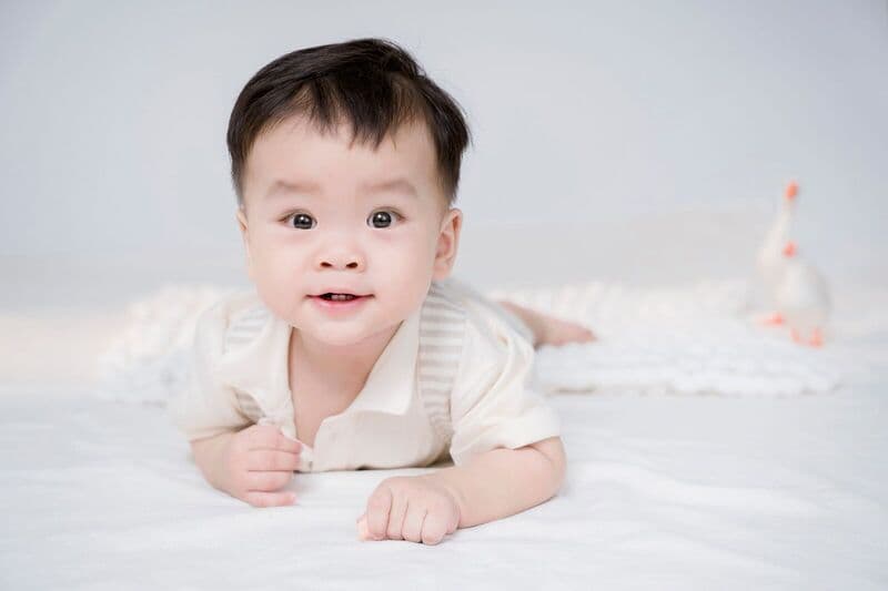Delizioso bambino sdraiato su una morbida coperta bianca durante un servizio fotografico in studio, catturando gioia e innocenza.