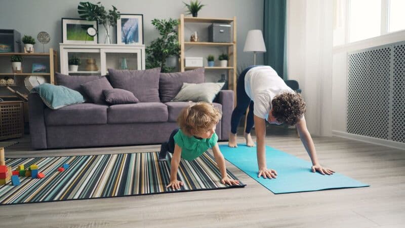 Una madre e suo figlio praticano yoga insieme in un accogliente soggiorno. Fitness familiare a casa.