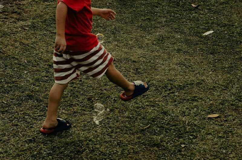 Bambino che cammina sull'erba con pantaloni corti a righe rosse e ciabatte all'aperto