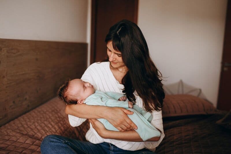 Una madre culla amorevolmente il suo bambino che dorme in una camera da letto confortevole, irradiando calore e affetto.