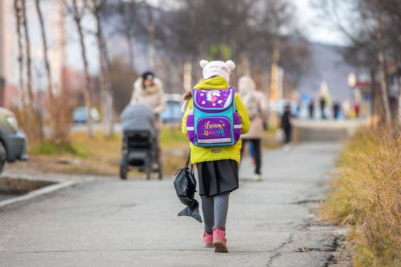 Un bambino che cammina per una strada con uno zaino vivace, catturando l'essenza dell'autunno.