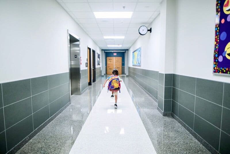 Un bambino corre in un luminoso corridoio scolastico, sottolineando l'architettura moderna e l'energia.