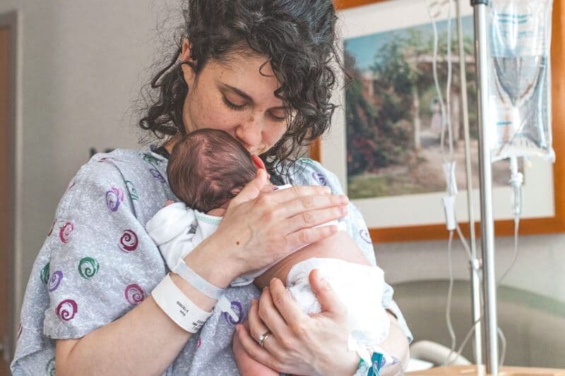 Madre che tiene dolcemente il neonato in un contesto ospedaliero, mostrando calore e amore.