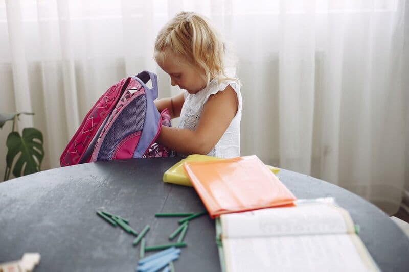 Una giovane ragazza prepara il suo zaino a casa, circondata da materiale scolastico, pronta per andare a scuola.