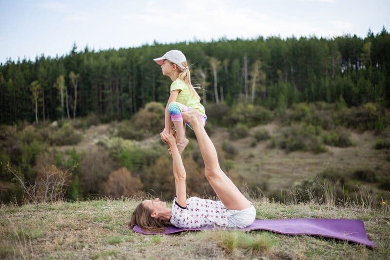 Una madre e una figlia si godono una posa di yoga insieme in un ambiente scenico all'aperto, dimostrando uno stile di vita sano.