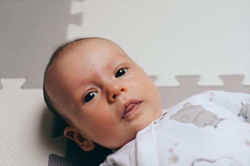 Bambino carino sdraiato su un tappeto da gioco a Poznań, con un'espressione facciale serena.