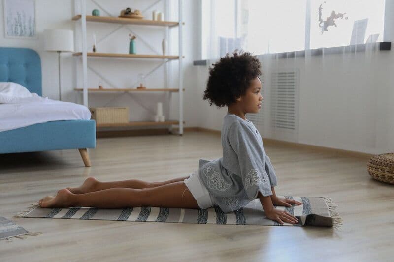 Bambina che pratica yoga in un ambiente interno sereno, focalizzandosi sul benessere e sulla consapevolezza.