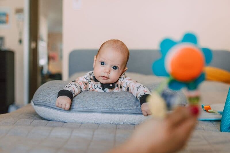 Bambino carino su un cuscino da letto che osserva un giocattolo colorato all'interno.