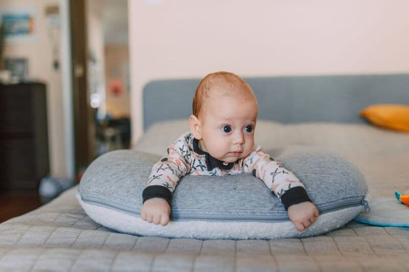 Incantevole bambino sdraiato a faccia in giù su un cuscino morbido in un accogliente ambiente interno.