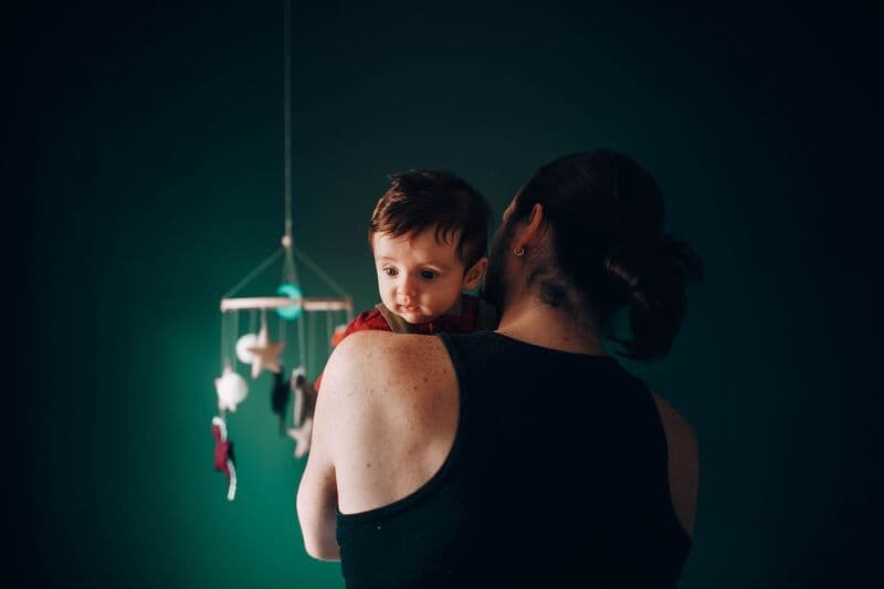 Un padre tiene il suo bambino in una stanza serena e debolmente illuminata, con un mobile appeso nei paraggi.