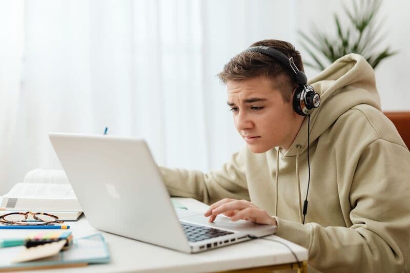 Adolescente con cuffie studia online con un laptop in un ambiente interno accogliente.