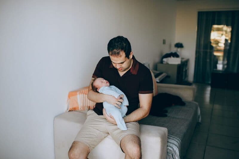 Un padre che stringe amorevolmente il suo neonato addormentato in casa, mostrando il legame e il calore della genitorialità.