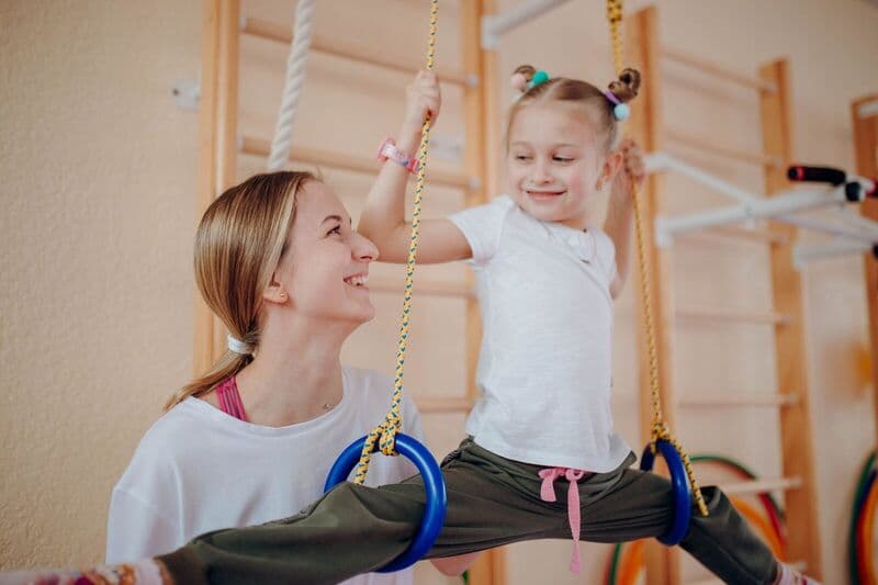 Una madre sorridente insegna alla figlia la ginnastica ai cerchi in casa, favorendo il legame e la flessibilità.