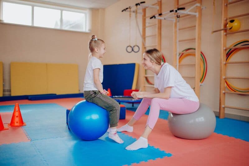 Madre e figlia felici che si legano su palle da esercizio in una palestra interna.