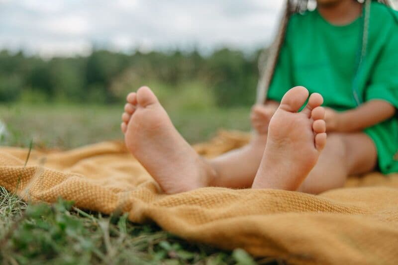Primo piano dei piedi di un bambino su una coperta da picnic all'aperto, godendosi una giornata di sole.