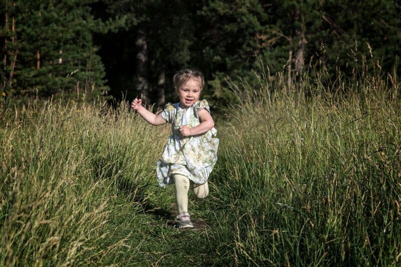Una bambina sorridente in un vestito floreale corre gioiosamente sull'erba verde in un prato soleggiato.