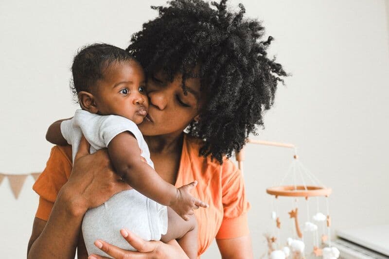 Una madre affettuosa bacia il suo bambino in un ambiente caldo e intimo, mostrando amore e connessione familiare.