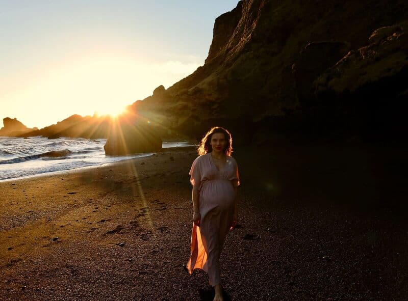 Una donna incinta in un abito fluido posa al tramonto sulla Spiaggia di Vík, Islanda.