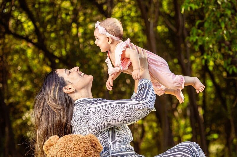 Madre e bambino condividono un momento di gioia all'aperto con una lussureggiante foresta verde sullo sfondo.