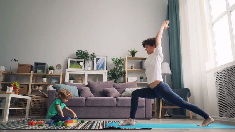 Una madre pratica yoga nel soggiorno mentre il suo bambino gioca con i mattoncini.