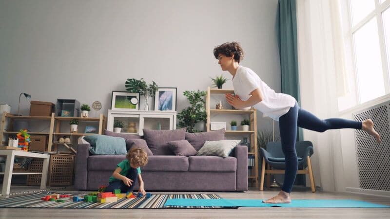 Una madre pratica yoga mentre suo figlio gioca con i blocchi in un accogliente soggiorno.
