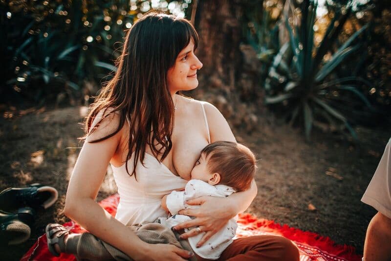 Una scena serena di una madre che allatta il suo bambino mentre è seduta su una coperta all'aperto in estate.
