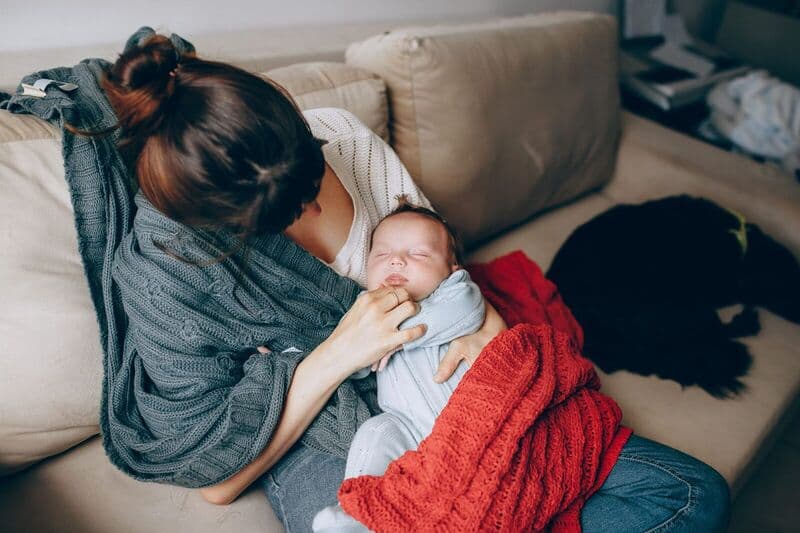 Un momento tenero di una madre che consola il suo bambino che dorme mentre riposa su un divano all'interno.