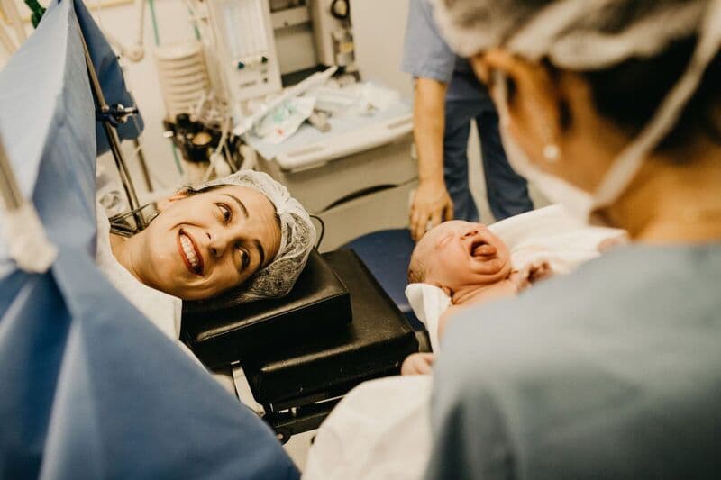 Una madre sorride affettuosamente al suo neonato in una sala parto dell'ospedale, assistita dallo staff medico.