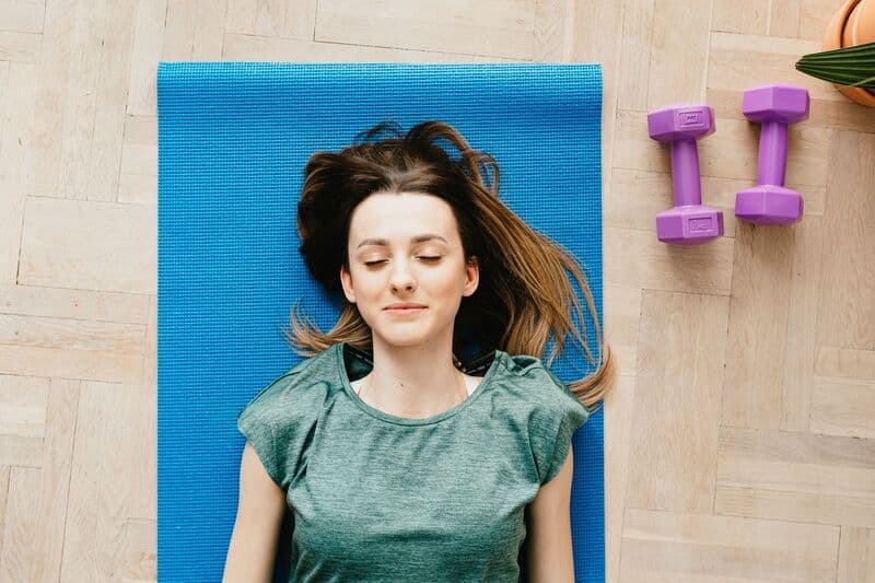 Una giovane donna che riposa pacificamente su un tappetino da yoga con pesetti accanto a lei, in casa.