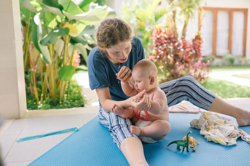 Una madre e il suo bambino giocano su un tappeto in un giardino soleggiato, godendosi del tempo di qualità insieme.