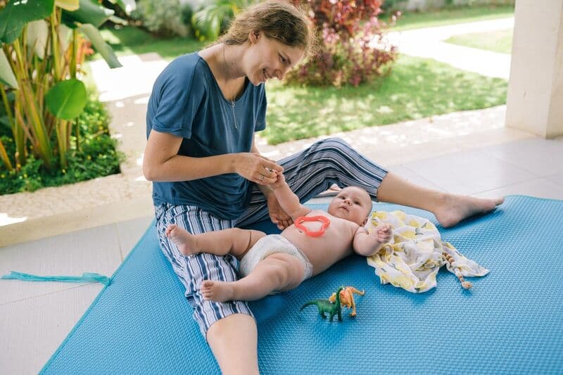 Madre sorridente e bambino giocano su un tappeto all'aperto, godendosi una giornata di sole con i giocattoli.