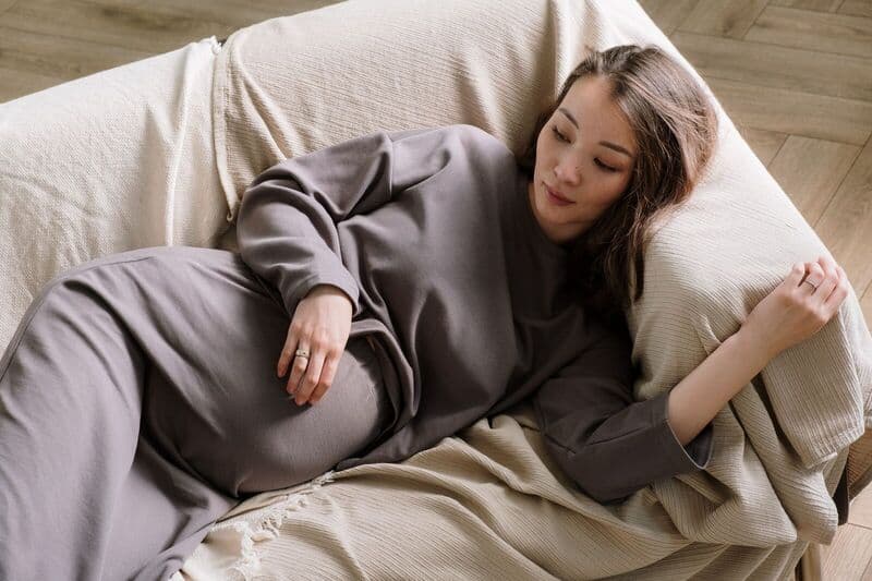 Donna incinta sdraiata su un divano comodo, abbracciando la calma e il relax.