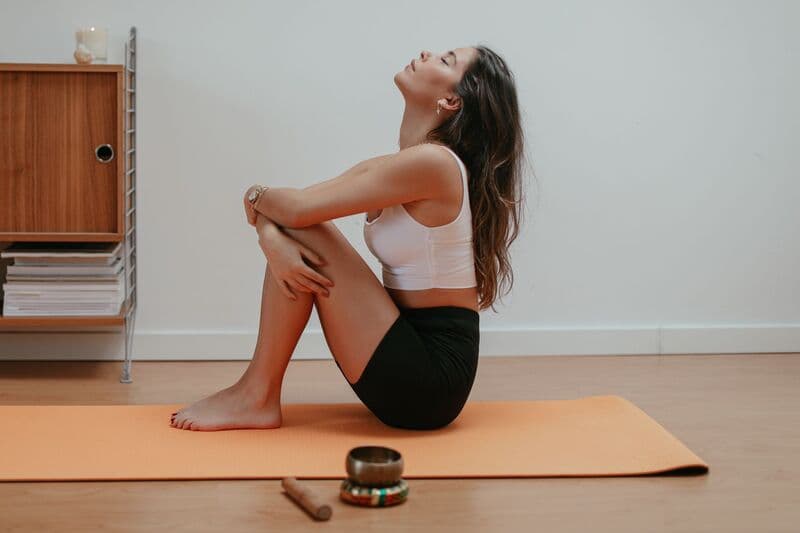 Donna che medita su un tappetino da yoga arancione all'interno, enfatizzando il relax e la consapevolezza.