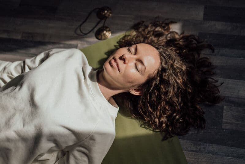 Donna con capelli ricci che medita sul tappeto da yoga al chiuso, occhi chiusi.