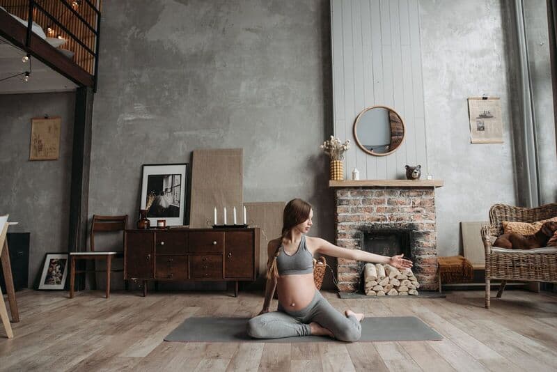 Donna incinta che pratica yoga in un'accogliente soggiorno con il suo cane vicino.