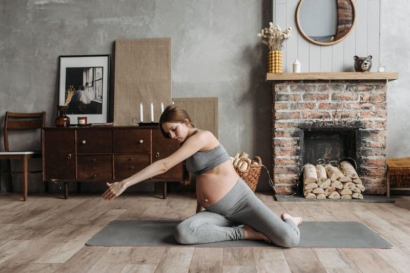 Donna incinta che pratica yoga a casa, concentrandosi sul benessere e sul rilassamento.