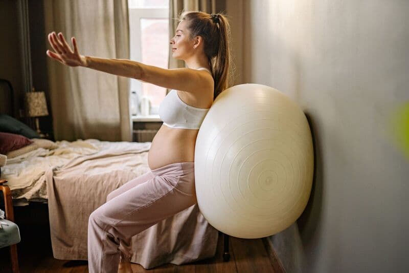 Donna incinta che pratica esercizi fitness a casa usando una palla di stabilità per una vita sana.