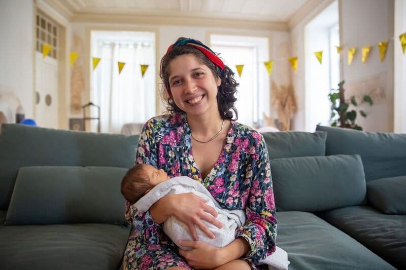Una madre sorridente culla il suo neonato in un accogliente soggiorno, mostrando amore e connessione familiare.