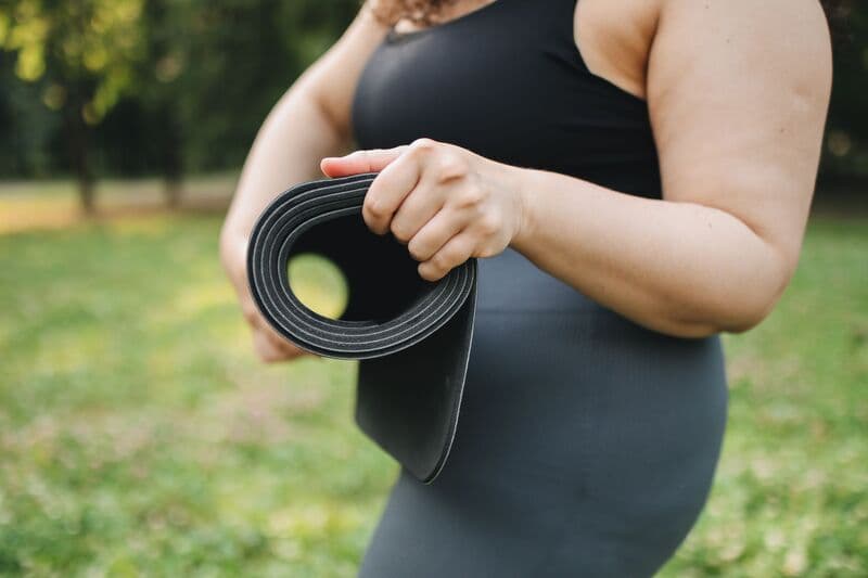 Primo piano di una donna che tiene un tappetino da yoga in un parco all'aperto soleggiato.