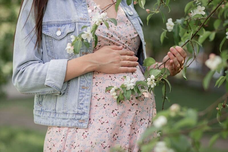 Donna incinta in un vestito floreale che tiene rami in fiore, simboleggiando nuova vita.