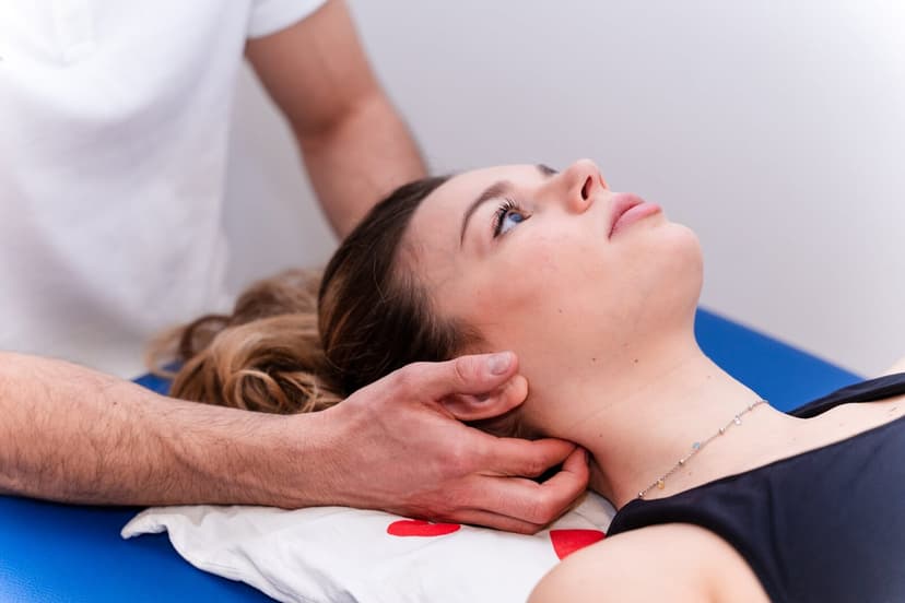 Paziente supina sul lettino blu con gli occhi aperti rivolti verso l'alto mentre le mani del fisioterapista le tengono il collo