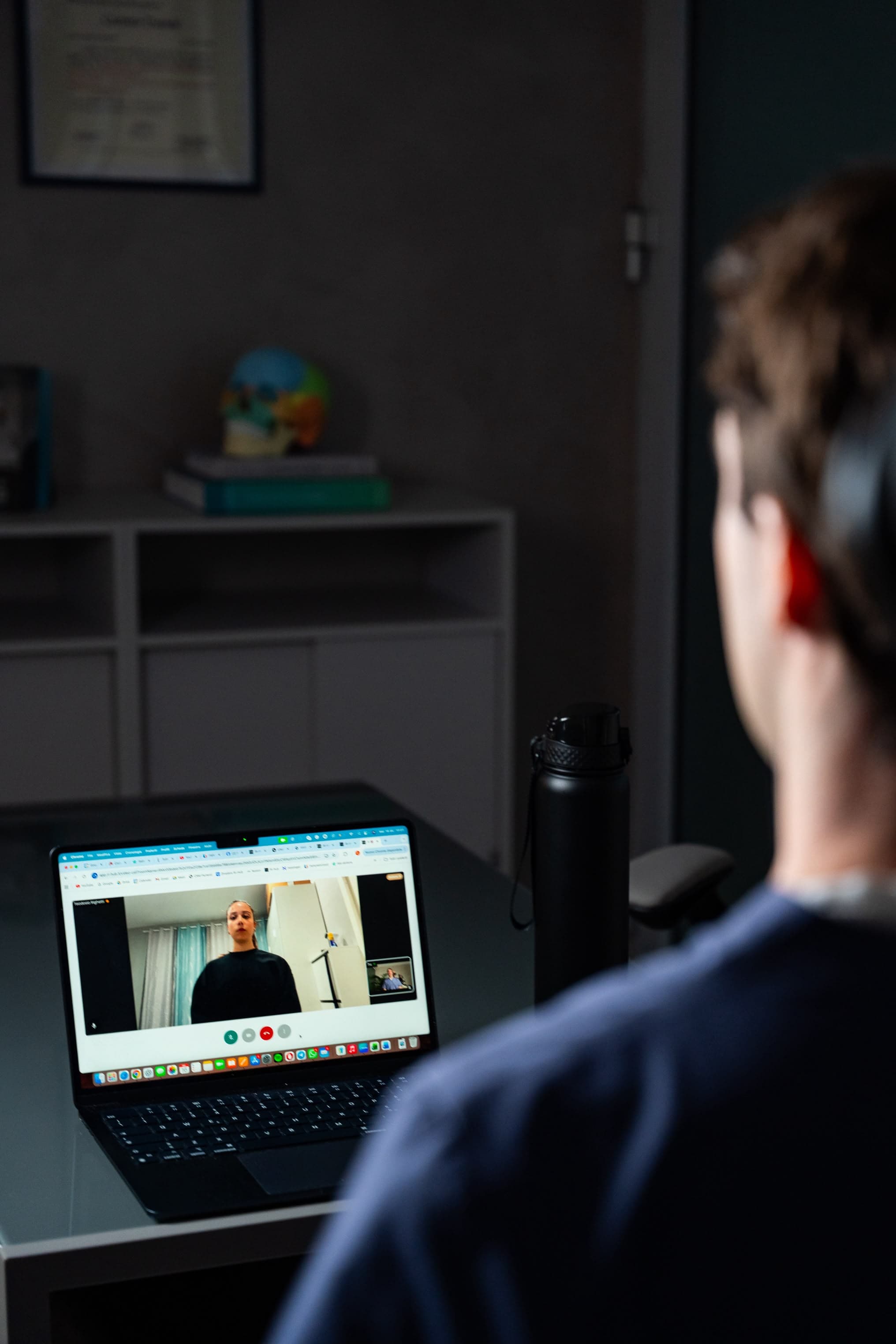 Un uomo di spalle, seduto davanti al laptop, segue la videochiamata con la fisioterapista che compare sullo schermo.