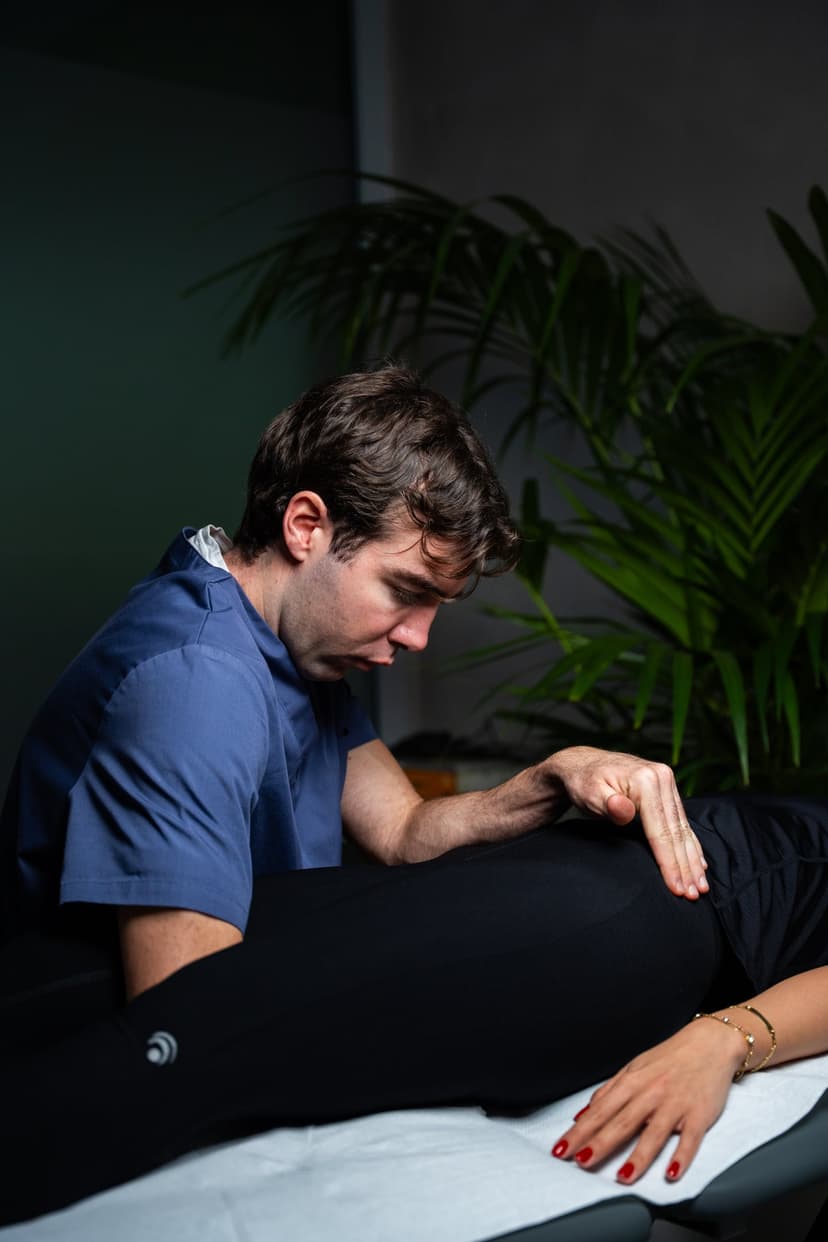 Il fisioterapista seduto accanto al lettino appoggia una mano sulla coscia della paziente distesa.