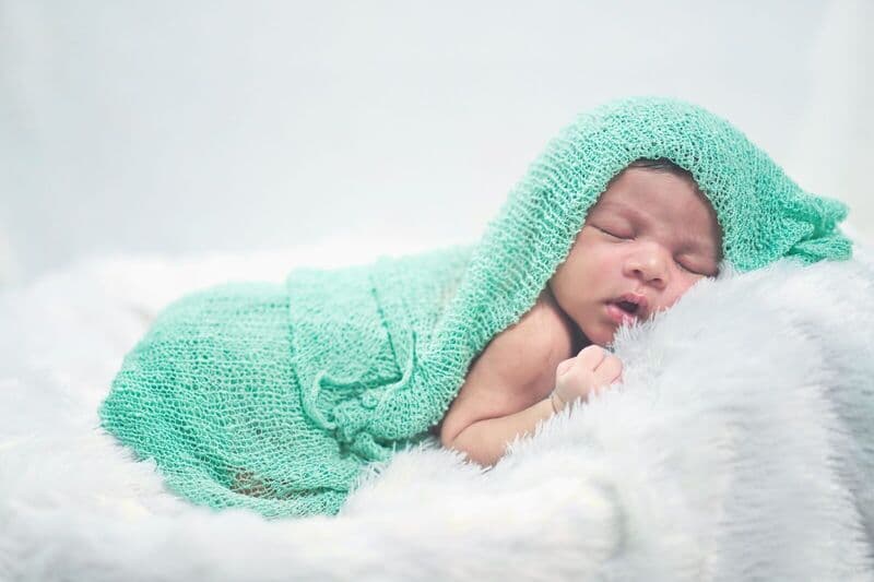 Immagine serena di un neonato avvolto in una morbida coperta verde lavorata a maglia, che riposa pacificamente.