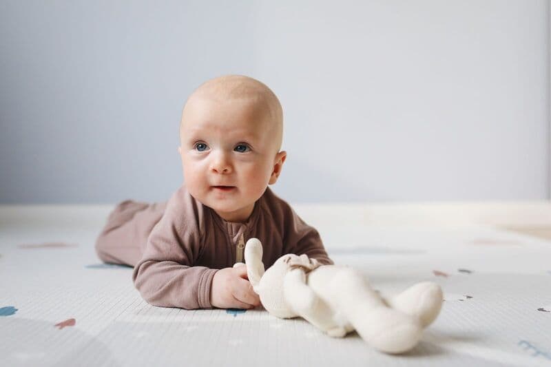 Bambino carino per terra con gioco di peluche, ambiente luminoso, focus sull'espressione facciale.