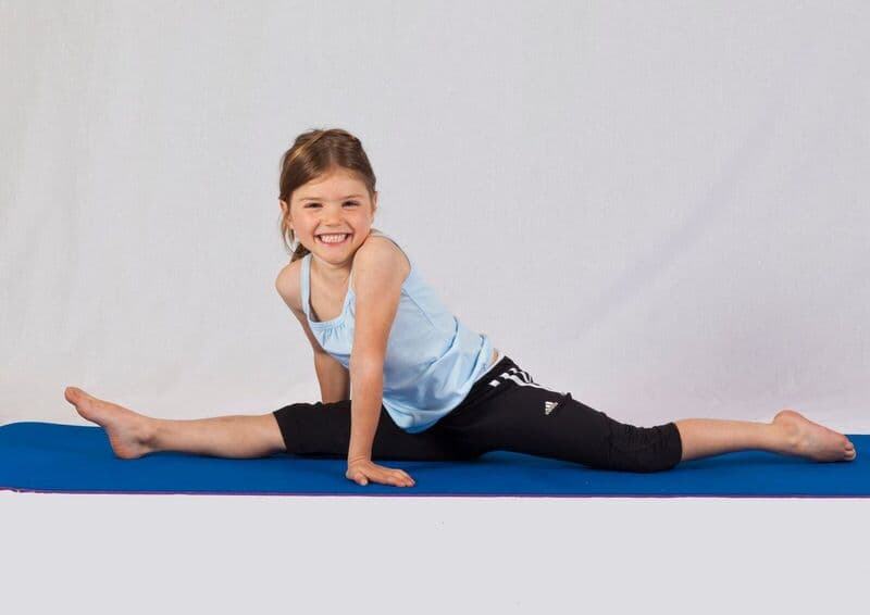 Giovane ragazza sorridente che esegue uno spagat su un tappetino da yoga in interno, mostrando flessibilità e gioia nell'esercizio.