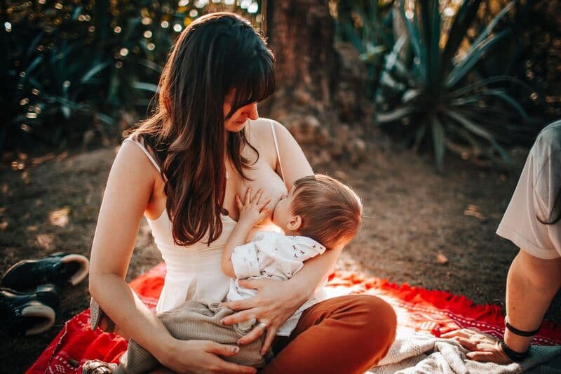 Donna che allatta il bambino all'aperto in una giornata di sole, mostrando cura e amore.