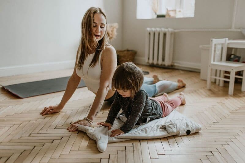 Una madre e un figlio che praticano yoga insieme a casa in una giornata di sole, promuovendo il benessere e la connessione.